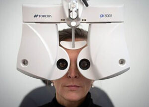 Close-up: Woman's face undergoing an eye exam using a white Topcon machine.
